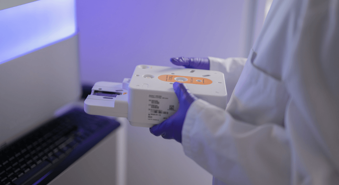 A lab technician holds a scientific device near a computer.