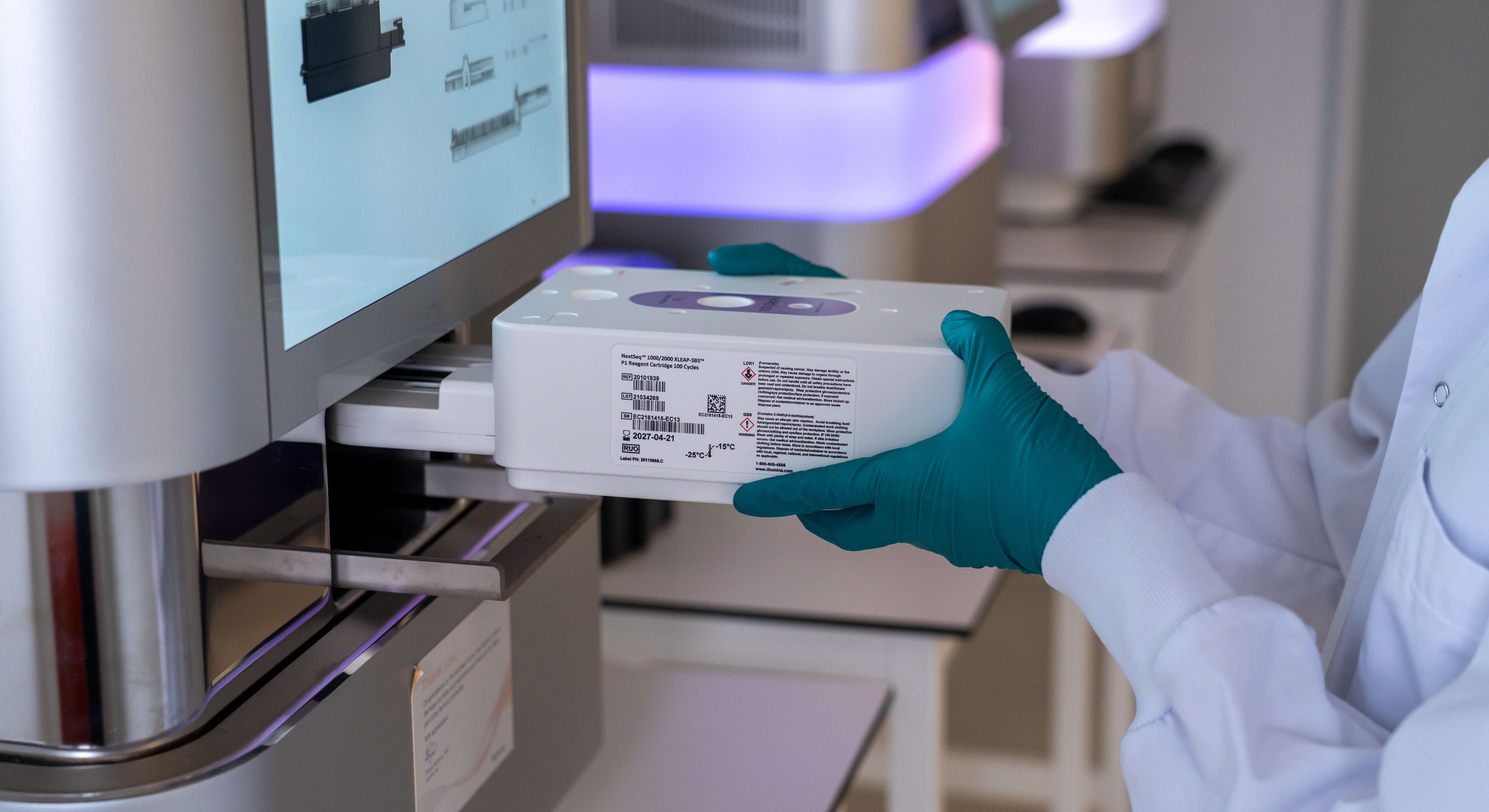 A lab technician holds a scientific device near a computer. Photo by: Emil Petersen